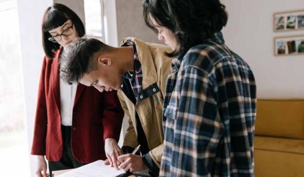 First-home buyer signing mortgage documents while discussing how a student loan may affect borrowing capacity